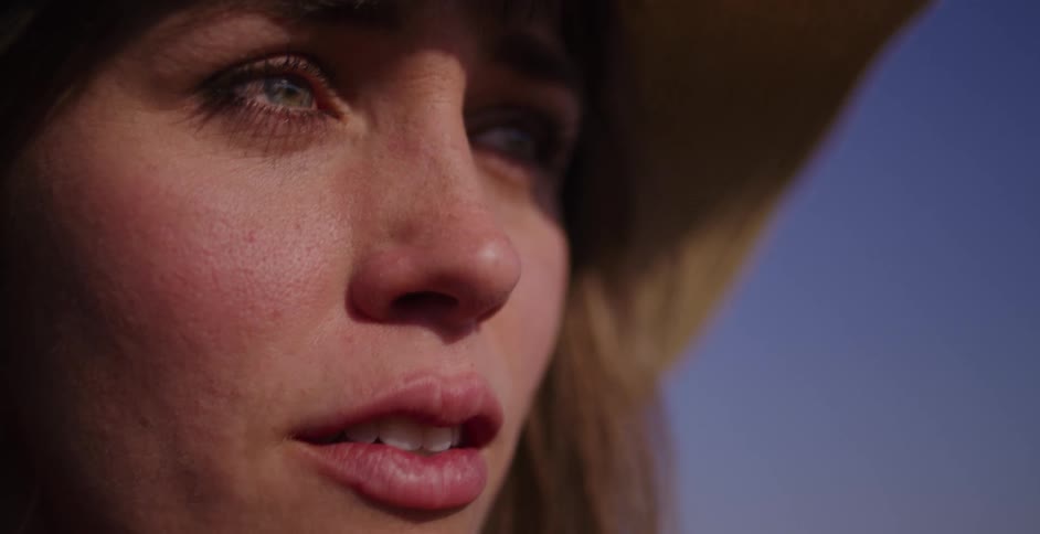 Close up of a beautiful young woman in a hat smiling peacefully as she slowly opens her eyes in the warm sunlight