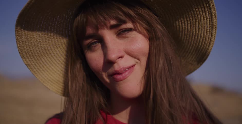 A peaceful young woman in a floppy straw hat smiles gently and closes her eyes, basking in the sunshine