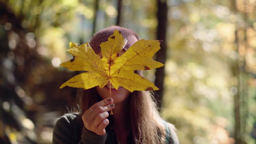 A woman holds a large yellow leaf up to her face