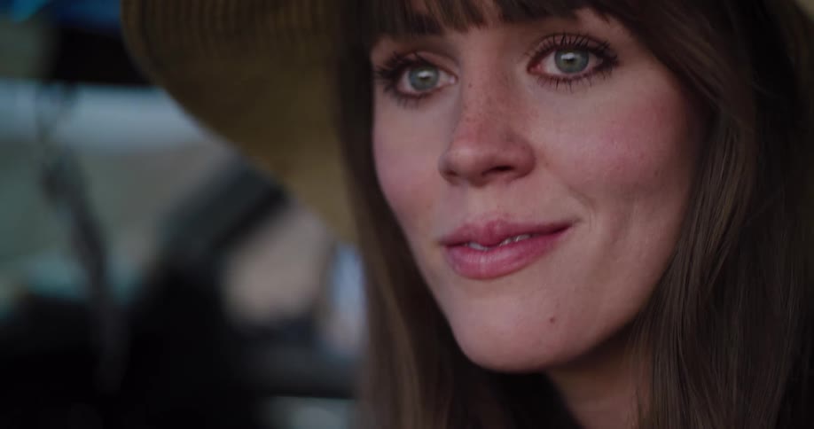 A slow motion close-up reveals the face of a beautiful young woman wearing a floppy straw hat, smiling gently in a car
