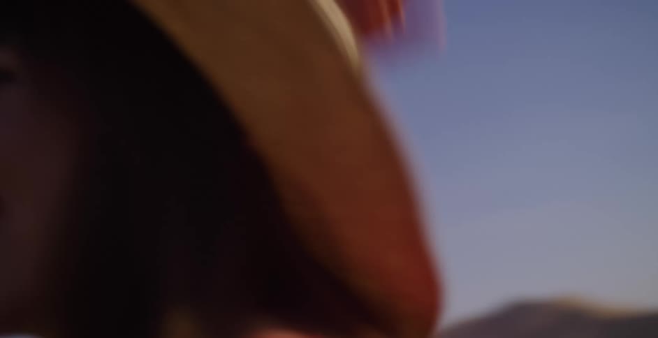A joyful woman in a straw hat laughs as she runs outdoors, her hair blowing in the wind under a sunny sky