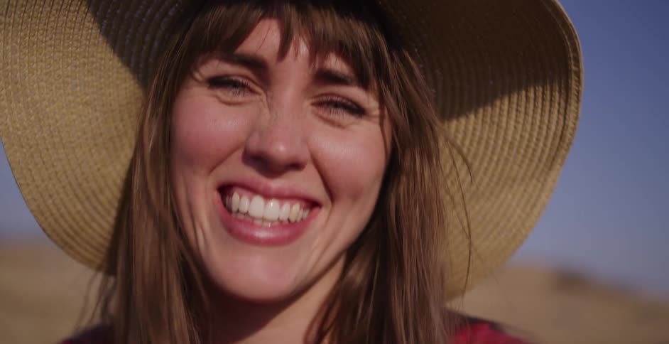 Slow motion close up of a beautiful woman with a big smile and a straw hat enjoying a sunny day outdoors