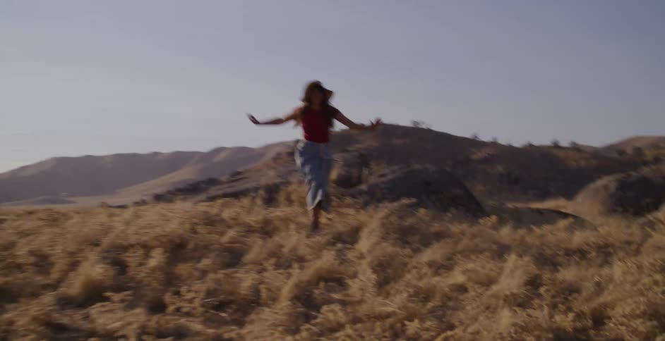 A joyful woman in a straw hat runs freely with her arms outstretched through a golden, sun-drenched field