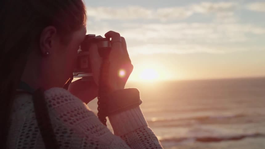 Woman taking a picture with camera of ocean at sunset on windy day