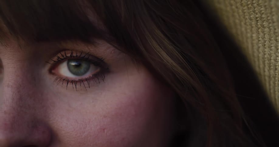 An intimate macro shot of a young woman's green eye blinking slowly in a moody and contemplative close-up