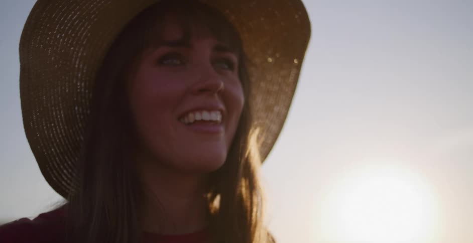 A happy woman in a hat takes a picture with her instant camera during golden hour, smiling as she enjoys the moment