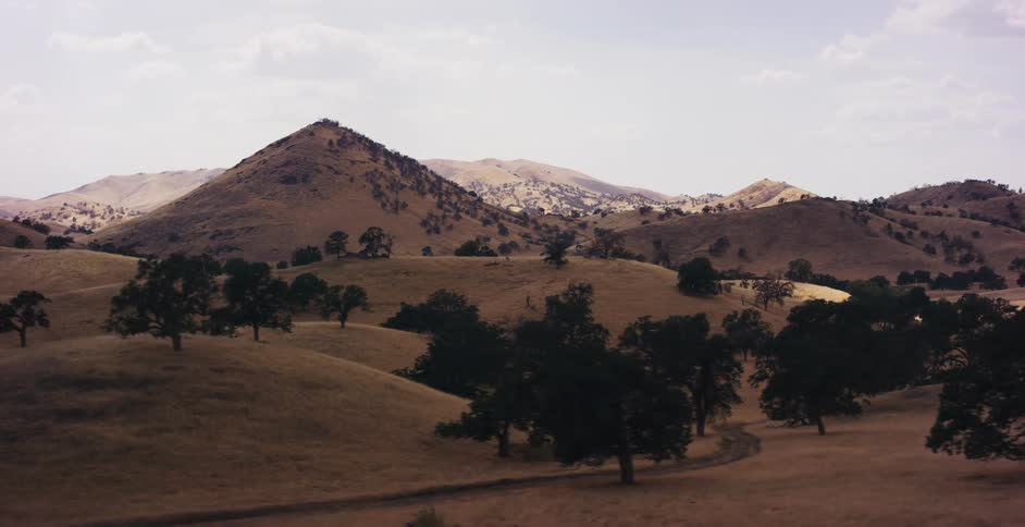 A slow, scenic tracking shot reveals the vast, golden rolling hills and scattered oak trees of a dry, rural landscape