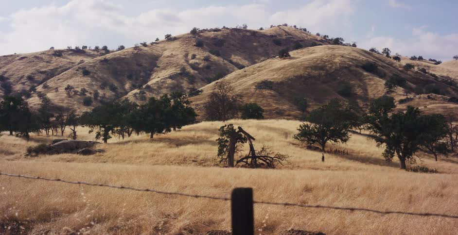 A sweeping pan across a vast, dry California landscape of golden rolling hills and scattered oak trees