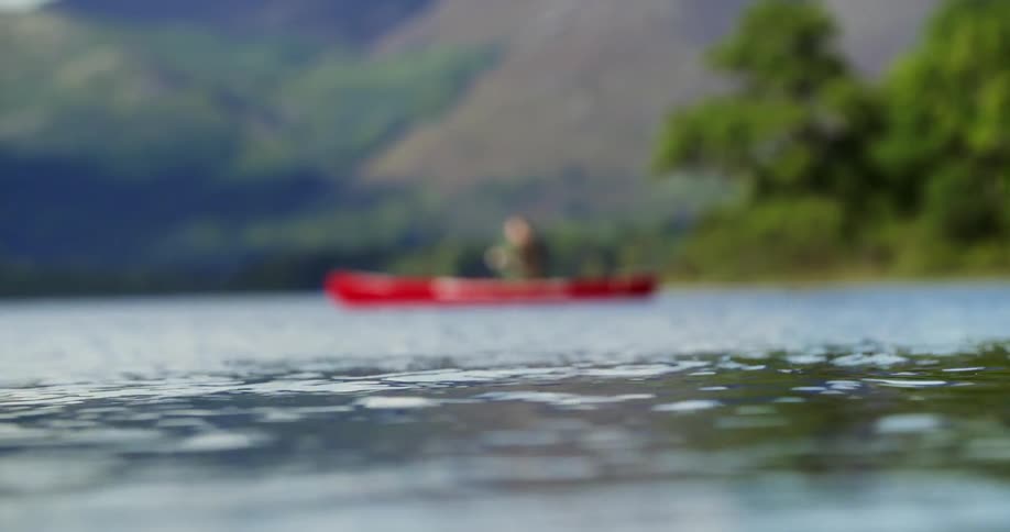 A person is paddling a canoe on a calm lake during the day