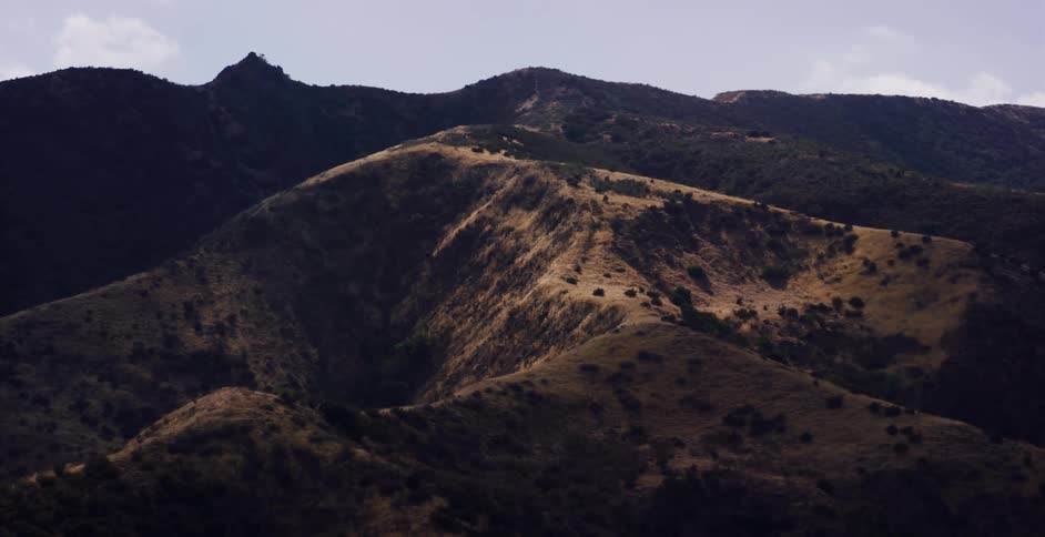 A moving viewpoint reveals the dramatic, rolling hills of a sunlit mountain landscape