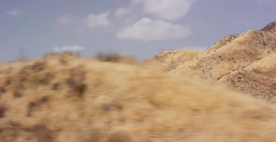 Slow motion parallax view from a moving vehicle of golden-brown desert hills with power lines on the horizon