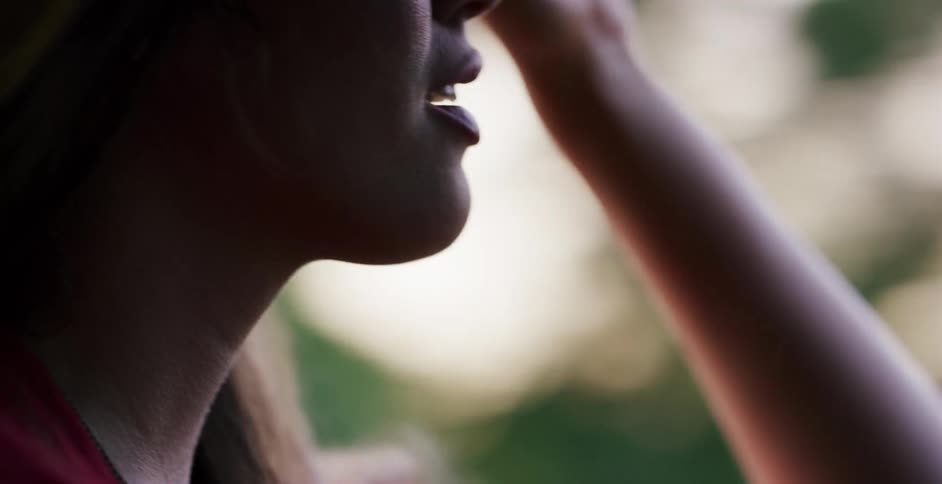 A close-up of a woman's mouth and chin as she exhales and watches the scenery from a moving vehicle