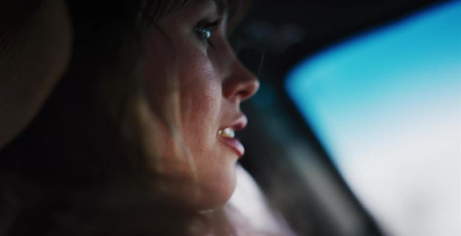Cinematic slow-motion close-up of a thoughtful woman's face as she drives, with her hair blowing in the wind