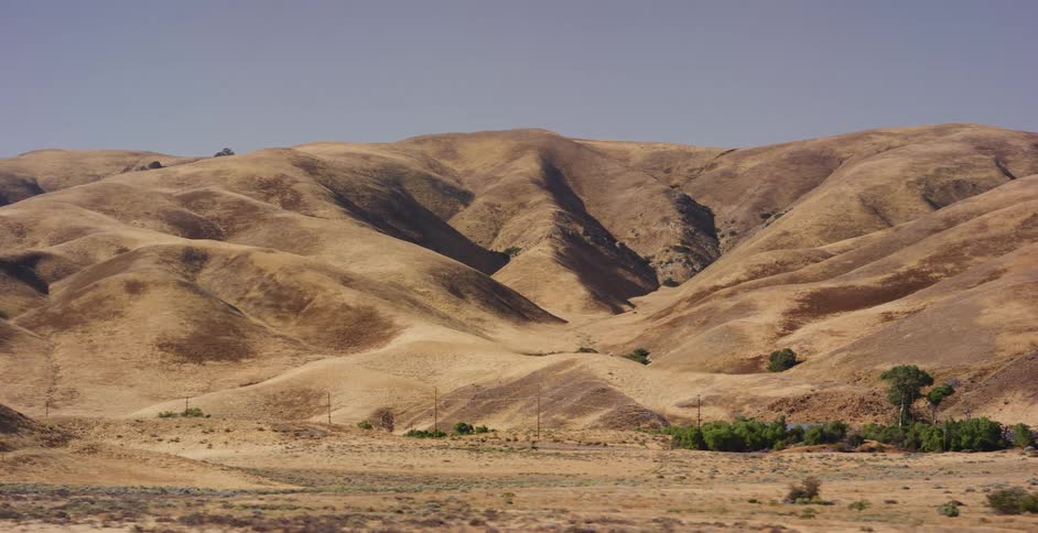 A scenic shot from a moving vehicle reveals the vast, dry golden hills of the California landscape