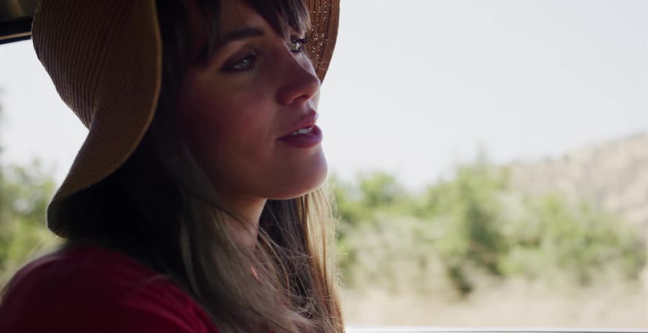 Serene woman in a straw hat gazes out the window while riding in a car on a bright day