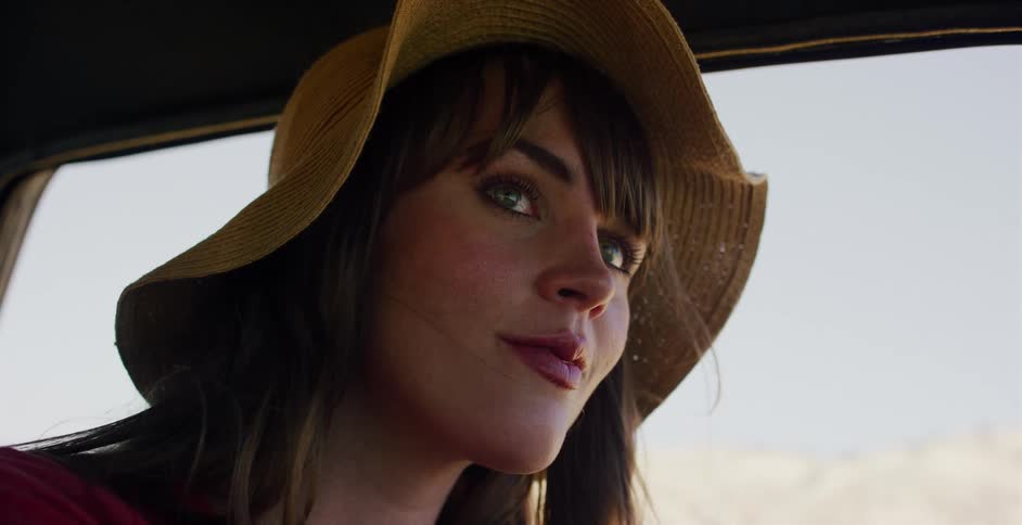 Close-up of a thoughtful woman wearing a straw hat looking out from her car on a sunny day road trip