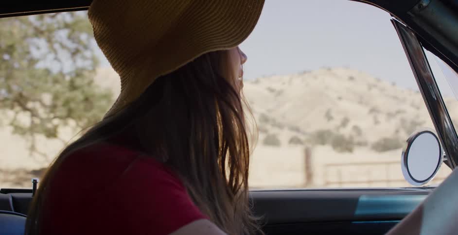 A stylish woman in a hat enjoys a sunny drive through the countryside in a classic car