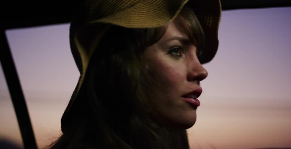 A stylish woman in a hat smiles while enjoying a peaceful car ride into the beautiful twilight sky