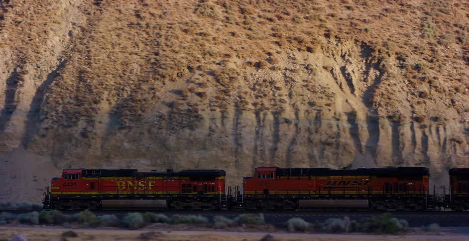 A BNSF freight train travels along a rocky desert bluff during the golden hour
