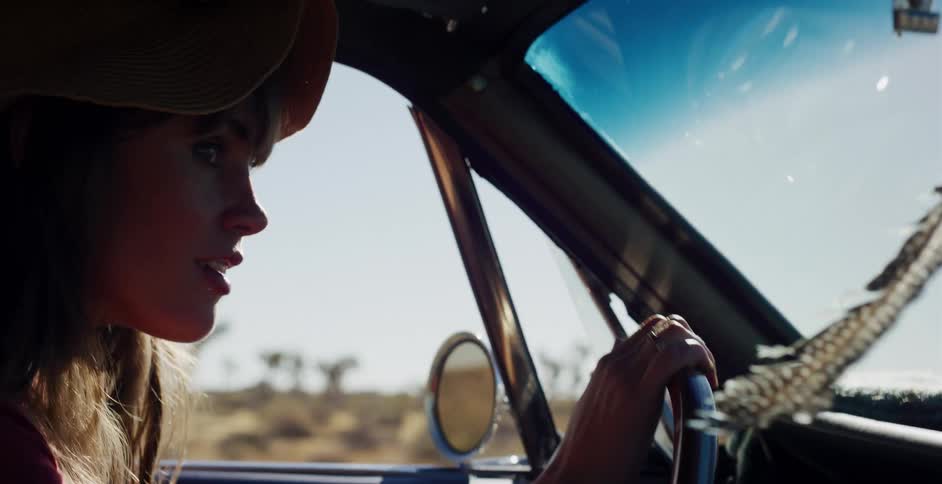 A stylish woman in a hat enjoys a sunny drive in a vintage car through the Joshua Tree desert
