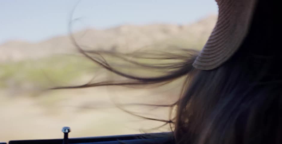 Close up in slow motion of a woman's hair blowing wildly in the wind as she drives through the desert on a road trip