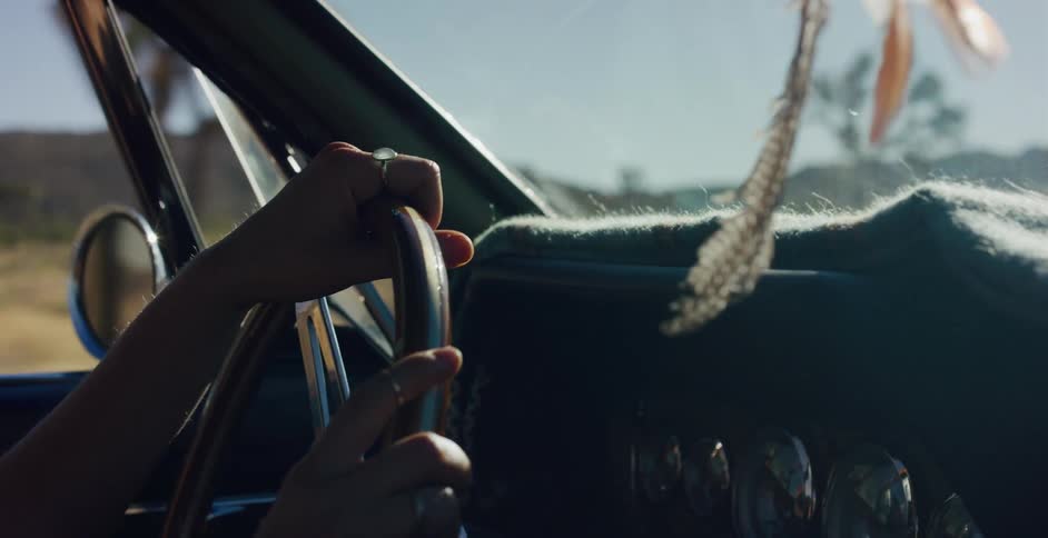 Slow motion close-up of a person's hands on the steering wheel of a vintage car while driving through a sunny desert landscape