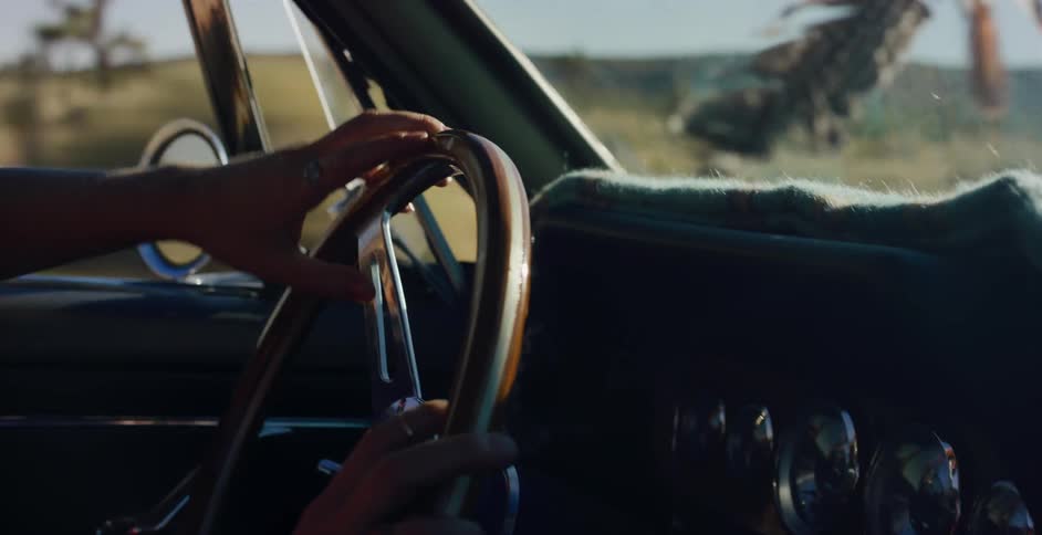Close up shot of a woman's hands on the steering wheel as she drives a vintage convertible down a desert road in slow motion