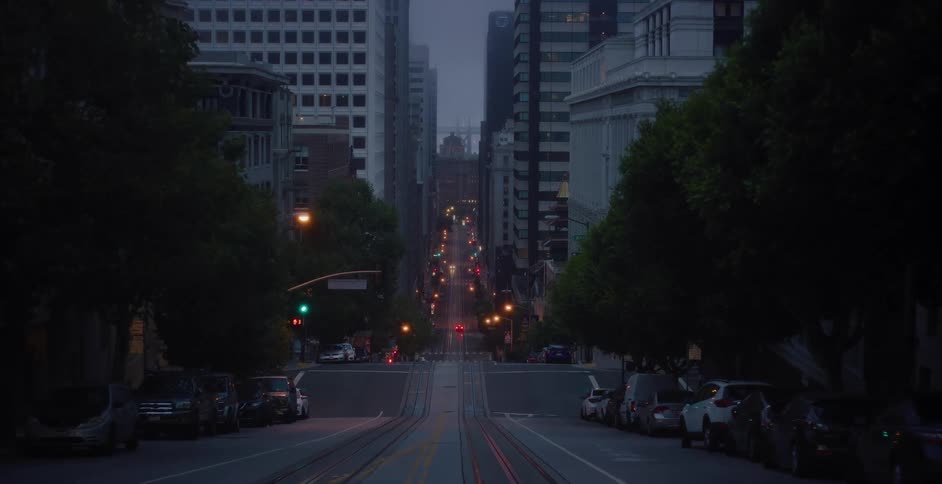A moody, atmospheric view looking down a quiet San Francisco street with glowing city lights at dawn