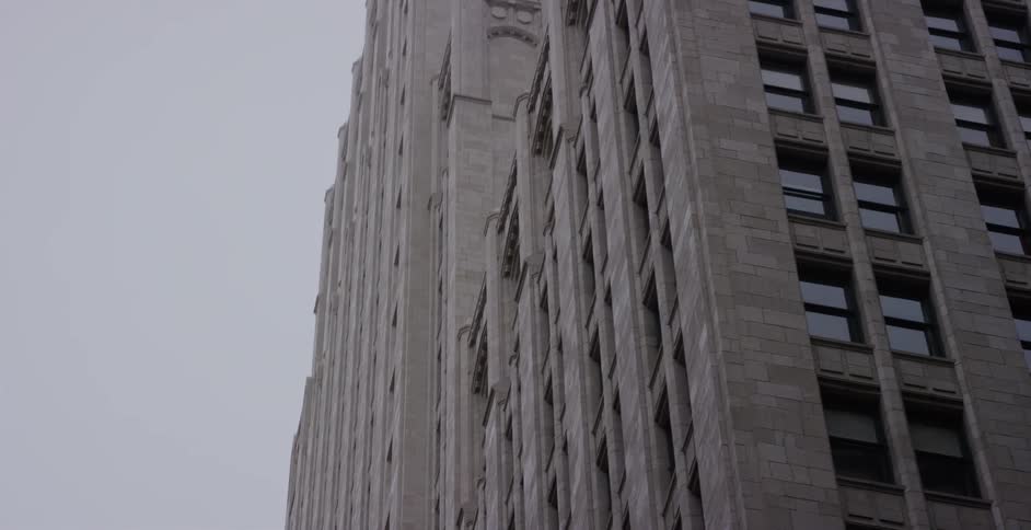 A slow, low-angle pan up the side of a vintage stone skyscraper on a grey, overcast day