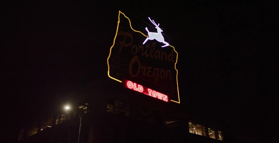 The iconic Portland, Oregon, Old Town neon sign glows brightly at night as the camera slowly pans across its facade