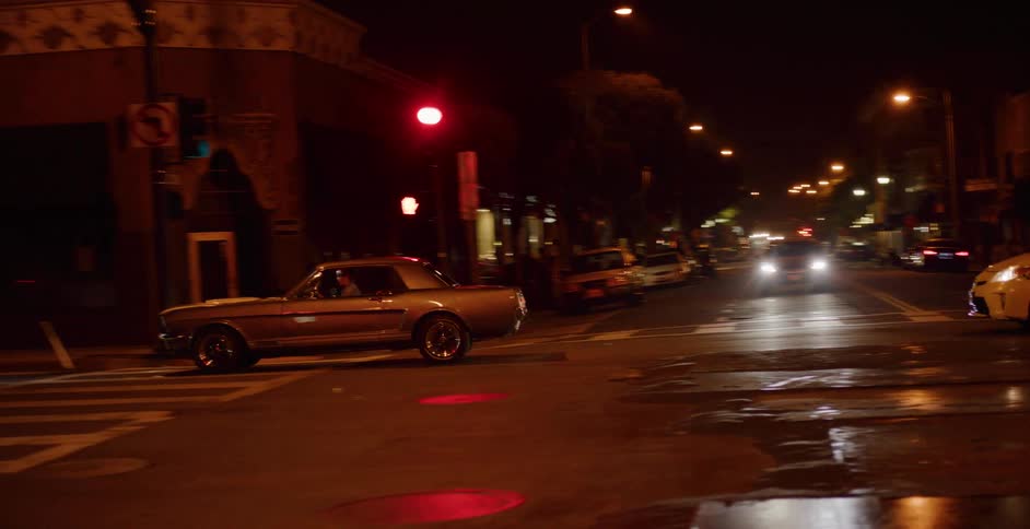 A classic gold Ford Mustang waits at a red light on a dark city street at night