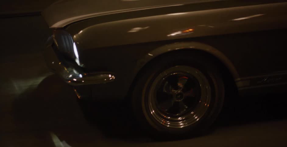 The gleaming headlights and chrome details of a classic muscle car are revealed in a slow pan at night