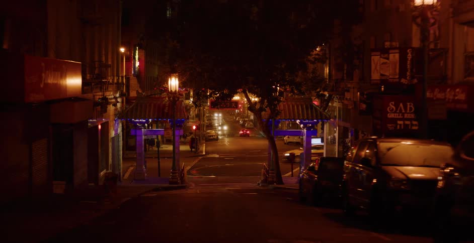 A slow pull-back shot reveals the iconic entrance gate to Chinatown at night, with city lights and distant traffic