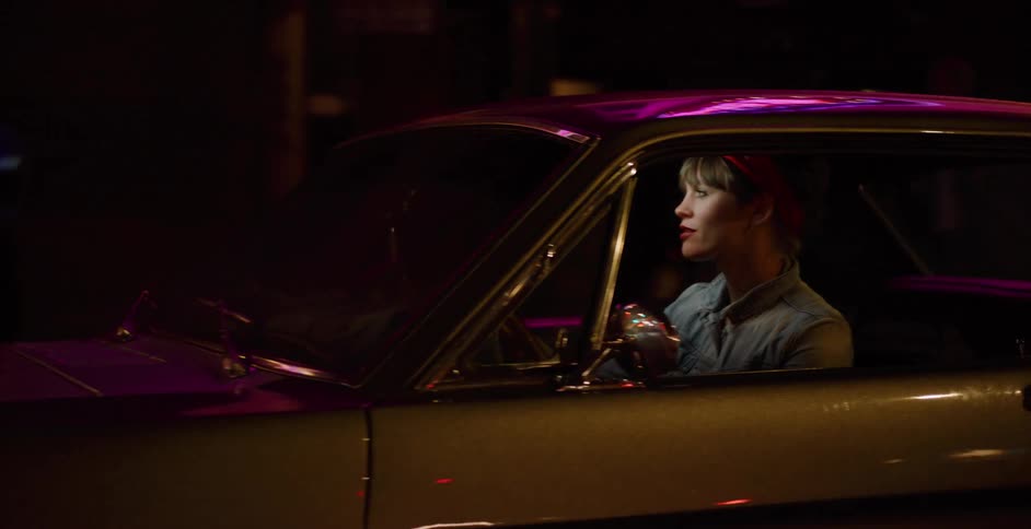 Tracking shot of a stylish woman in a red bandana driving a classic muscle car through a neon-lit city at night