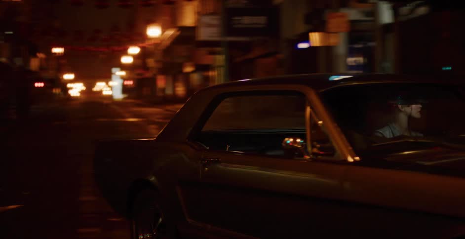 A woman drives a classic muscle car through a steamy, atmospheric Chinatown street at night