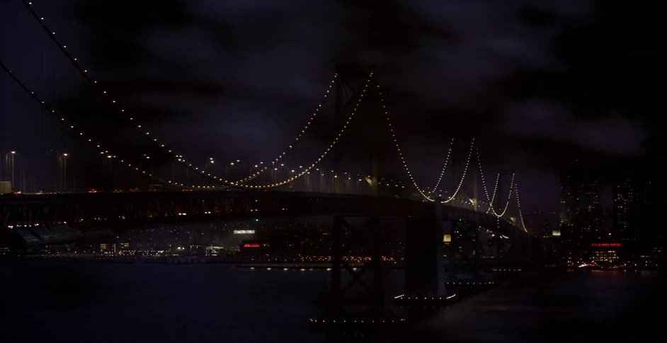 Dark clouds sweep across a dramatic panning time-lapse of the illuminated San Francisco Bay Bridge at night