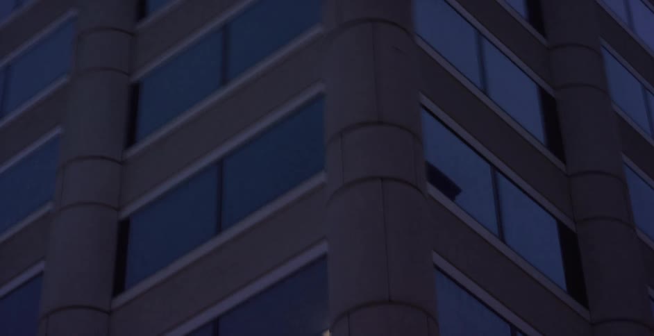 A slow, low-angle pan reveals the imposing facade of a modern skyscraper with reflective glass windows at dusk