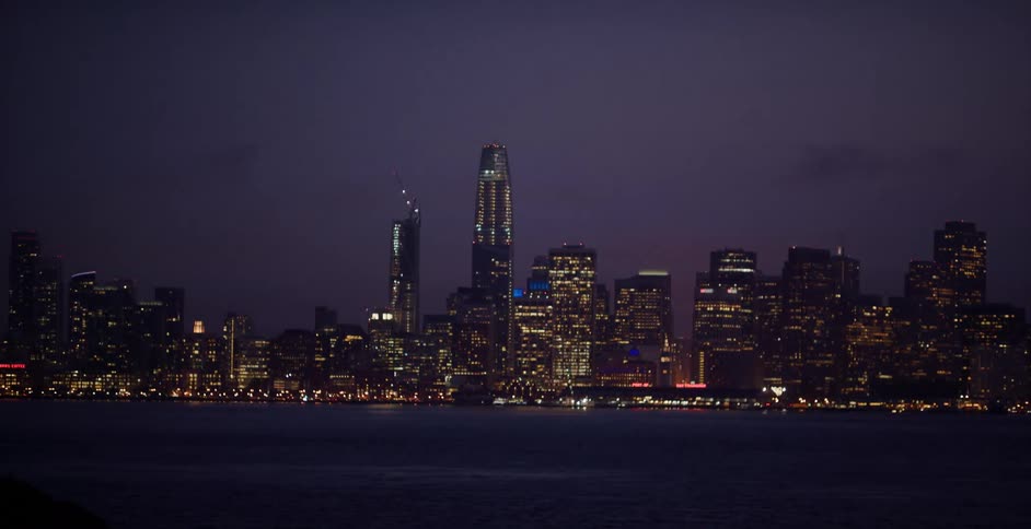 The iconic San Francisco skyline glimmers with city lights at dusk as seen from across the bay