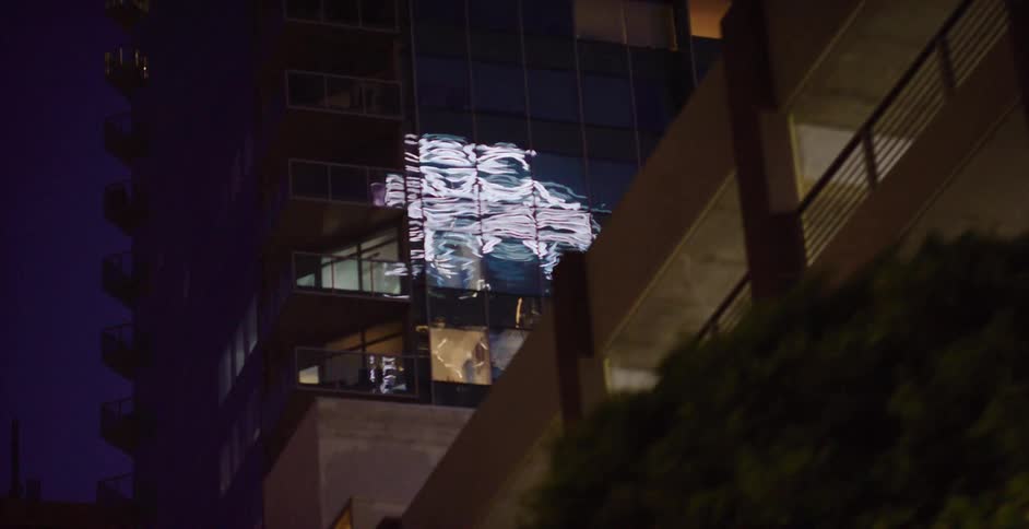 Rippling city lights reflect off a modern skyscraper's glass facade at night