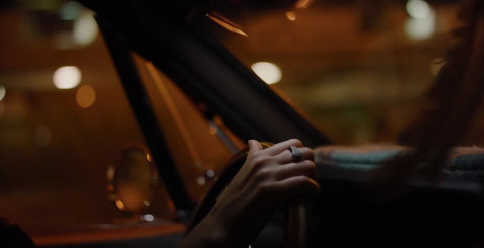 Close-up of a person's hand resting on a classic wooden steering wheel while driving through a city at night
