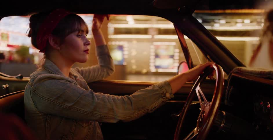 A stylish woman with a red bandana drives a classic car through the neon-lit city streets of Las Vegas at night