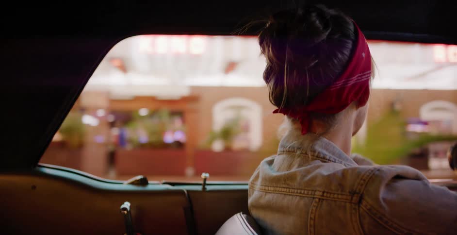 A stylish woman with a red bandana enjoys a slow drive in a vintage car through the dazzling neon lights of Las Vegas at night