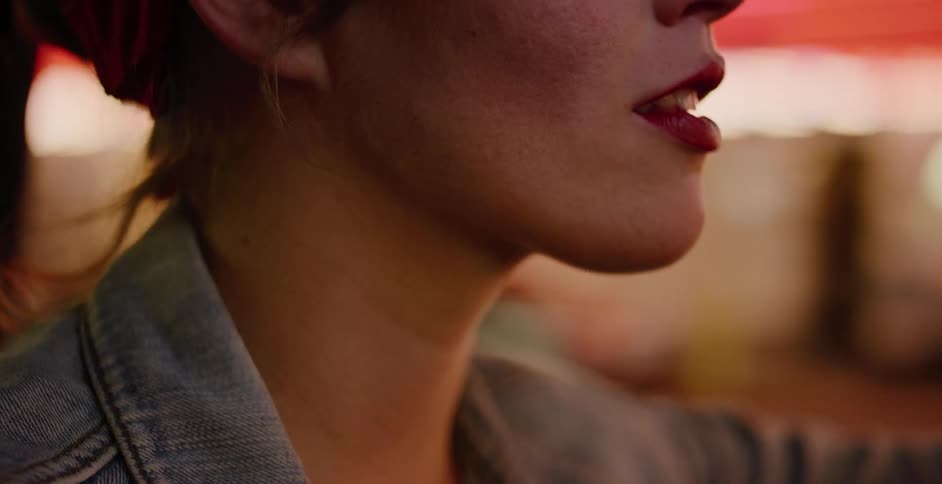 Cinematic close-up on a woman's mouth with red lipstick as she drives through the city at night with bokeh lights in the background