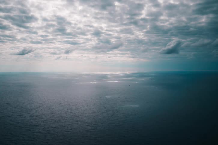 A vast and serene open ocean landscape is illuminated by sunbeams breaking through a dramatic, cloudy sky