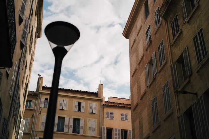 A slow pull-back shot looks up from a narrow European street at classic apartment buildings and a blue sky with soft white clouds