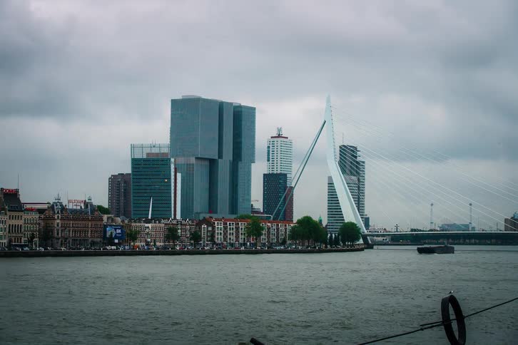 A timelapse of boats and water taxis moving along the Nieuwe Maas river in front of the Rotterdam city skyline on an overcast day