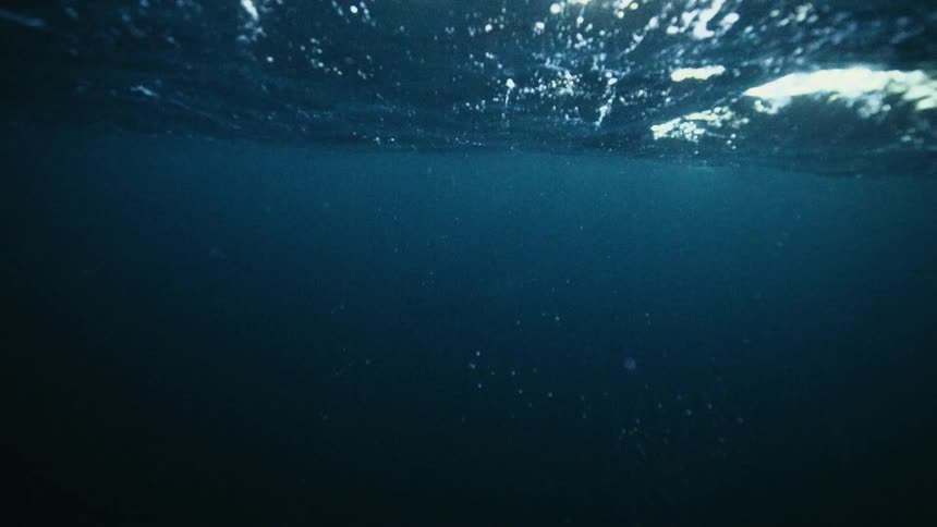 Slow motion underwater view of the dark, rippling surface of deep blue water