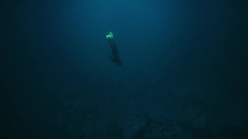 A serene free diver with bright fins slowly descends into the mysterious deep water