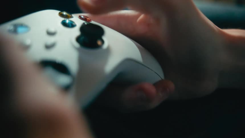 Close-up cinematic shot of a person's tattooed hands skillfully maneuvering a white video game controller in a dimly lit room