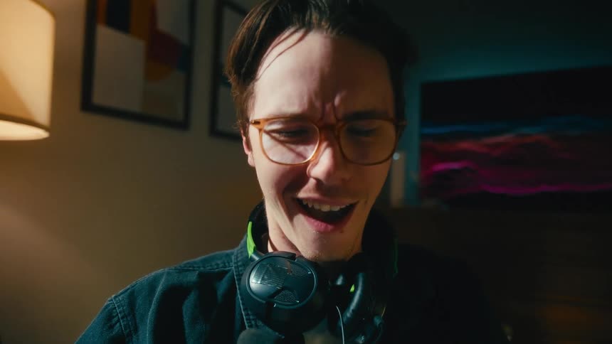 A dynamic close-up of an expressive young man in glasses reacting to his phone, going from a shocked shout to hysterical laughter
